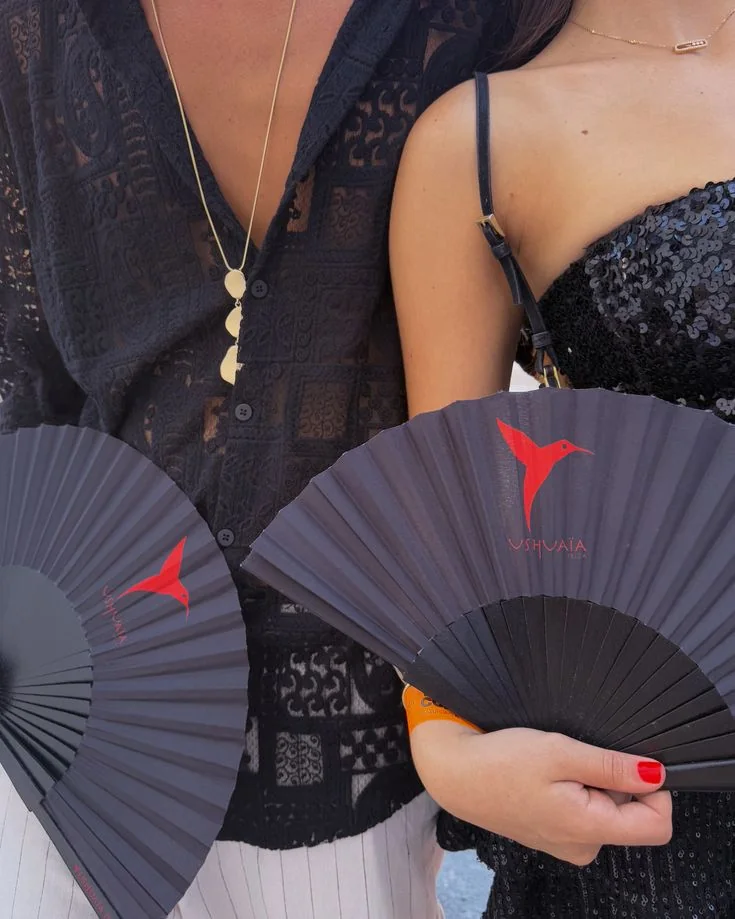 Dos abanicos negros personalizados con un colibrí rojo y el logo Ushuaïa